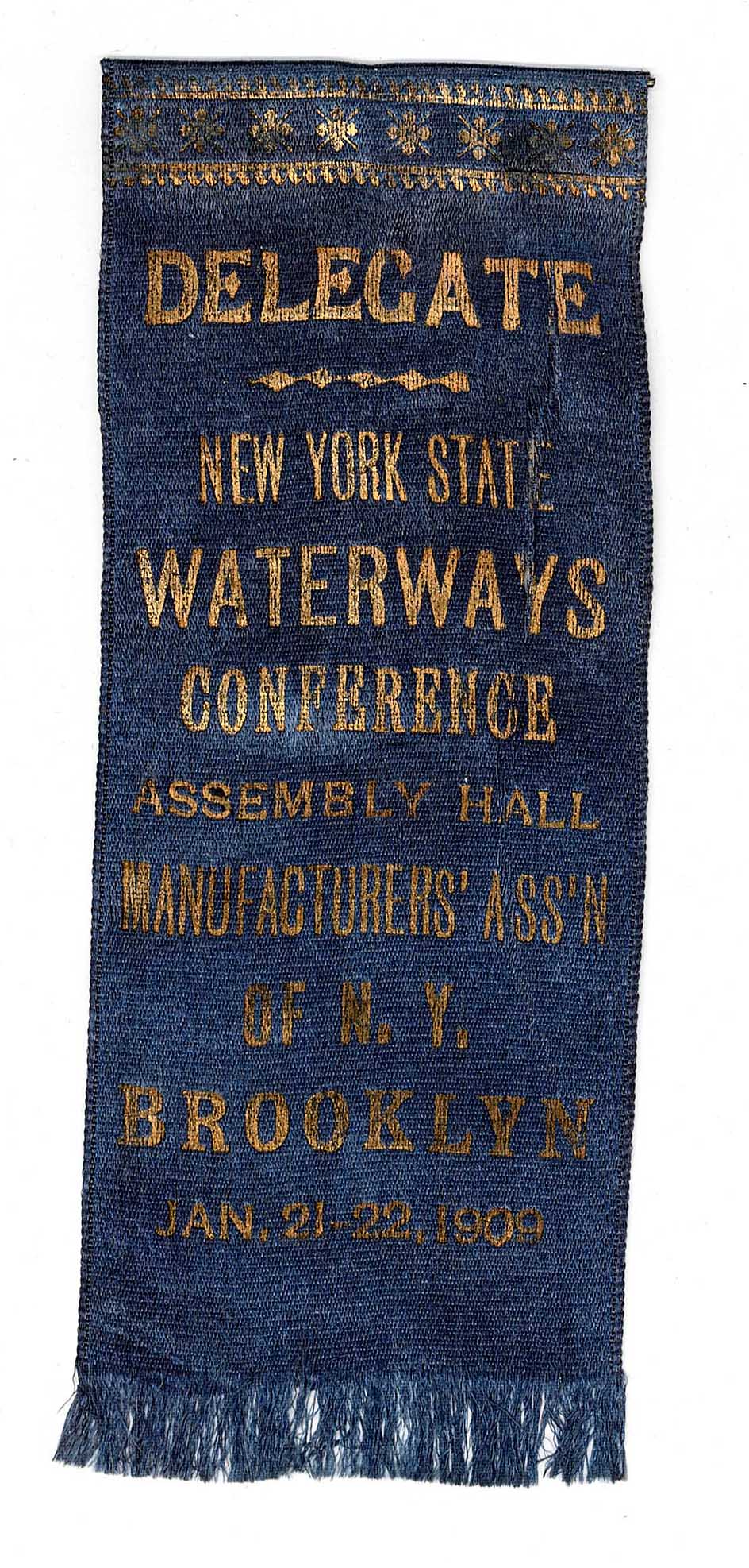 A blue ribbon with gold lettering, delegate to a waterways conference 1909